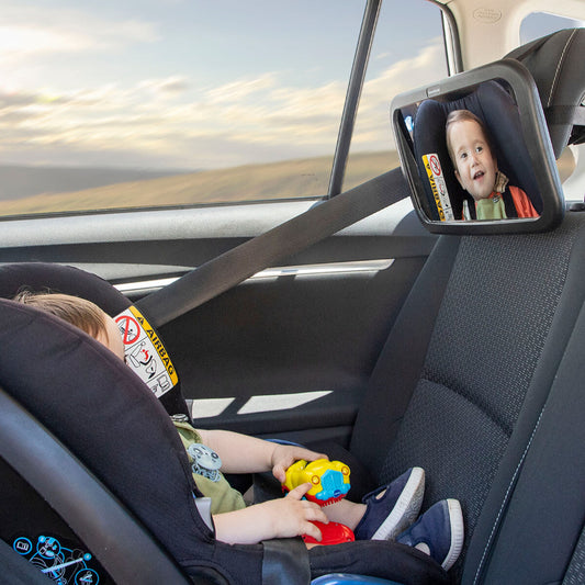 Child in a car seat with a toy, looking into a baby mirror showing a child's reflection.